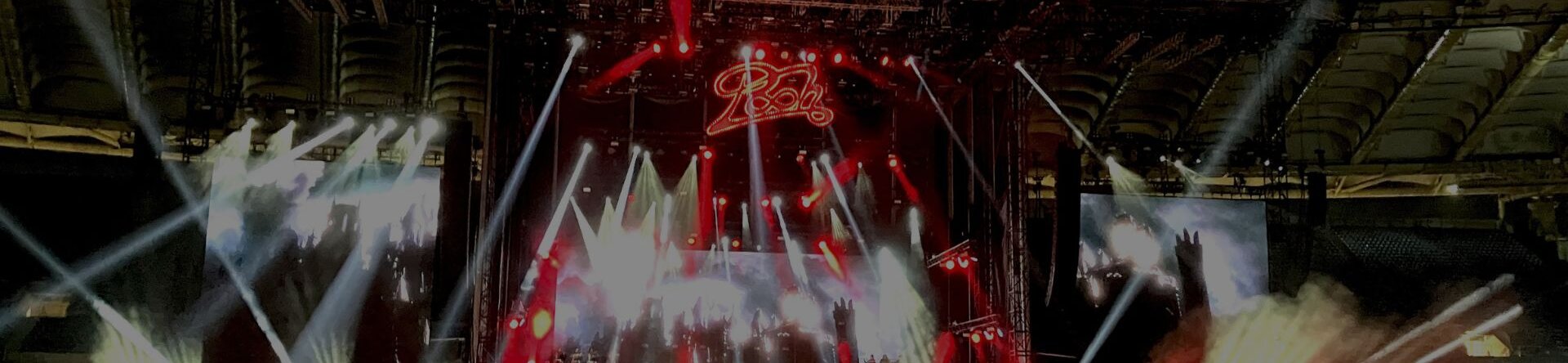 Grande pubblico al concerto dei Pooh 2023, palco scenografico con luci rosse e show visivo coinvolgente