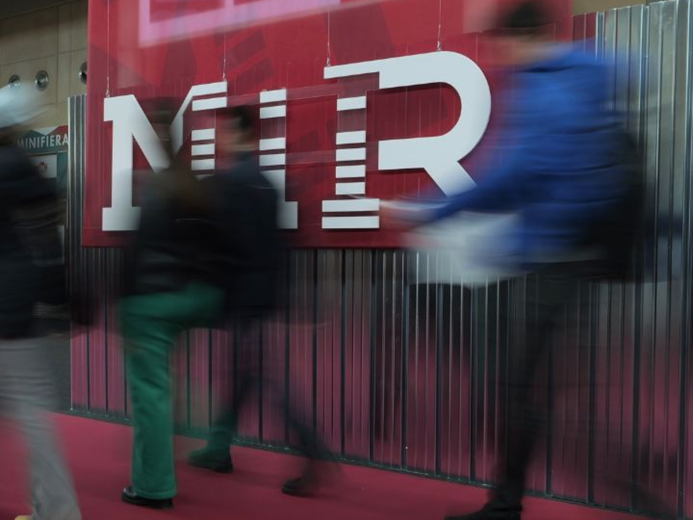 Persone in movimento all’ingresso dell’evento MIR con il logo in primo piano Ingresso evento MIR 2025