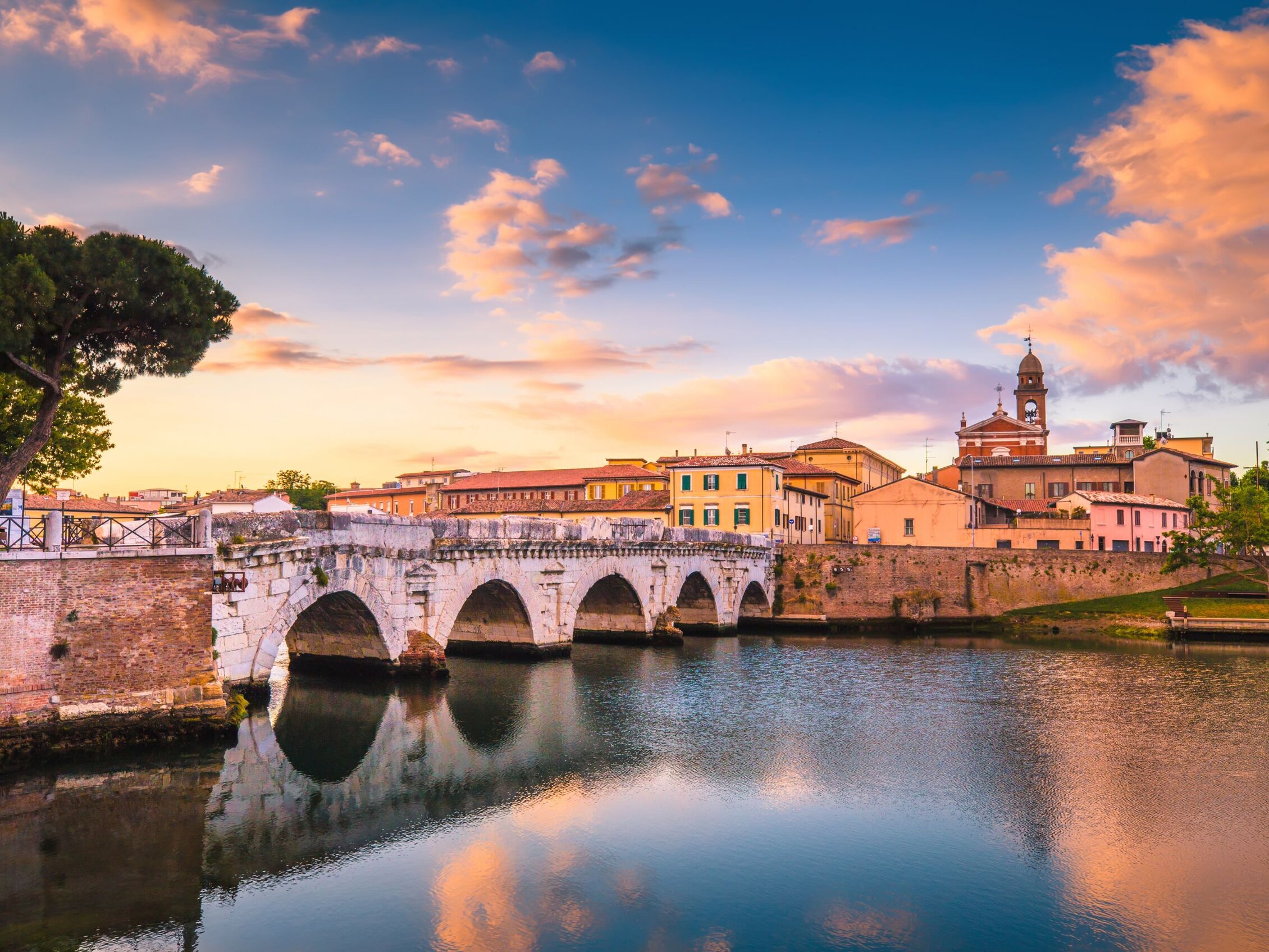 Ponte di Tiberio al tramonto Panorama del Ponte di Tiberio a Rimini al tramonto con riflessi sull’acqua e cielo colorato